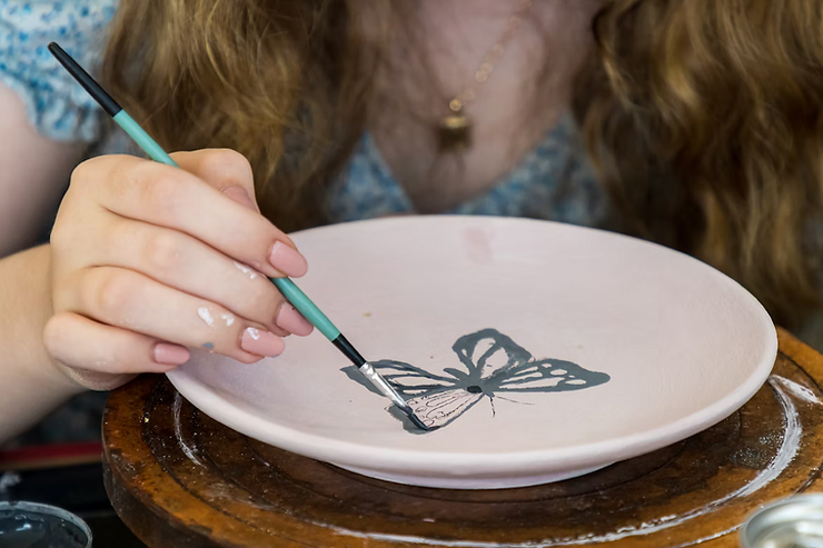 girl painting a butterfly on a pottery plate