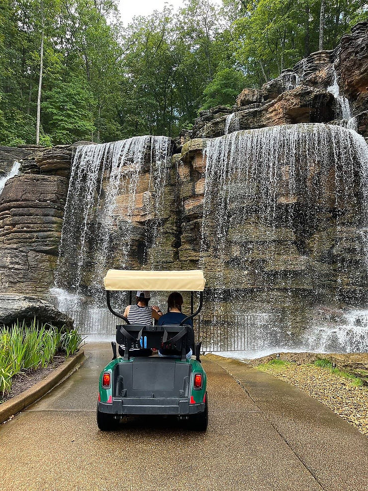 People riding in golf cart tour in front of waterfall at Top of the Rock in the Ozarks