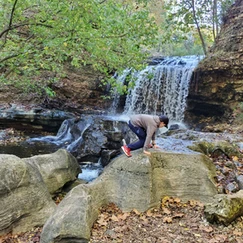 Teenager climbing rock with waterfall in background.